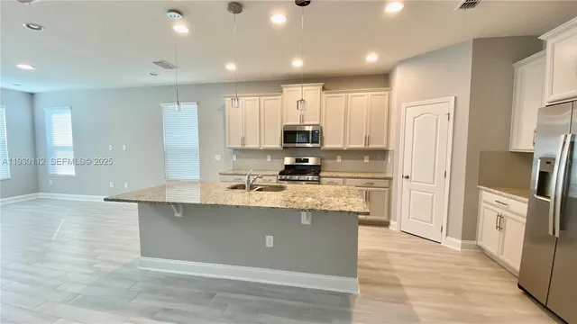 a large kitchen with stainless steel appliances granite countertop a stove a sink a refrigerator and white cabinets with wooden floor