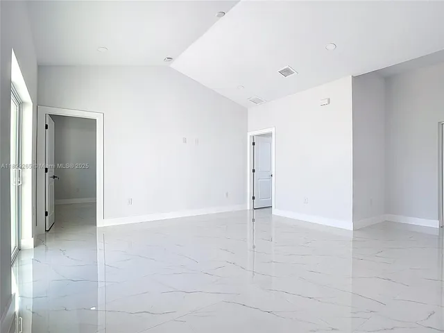 a view of an empty room with kitchen and a window