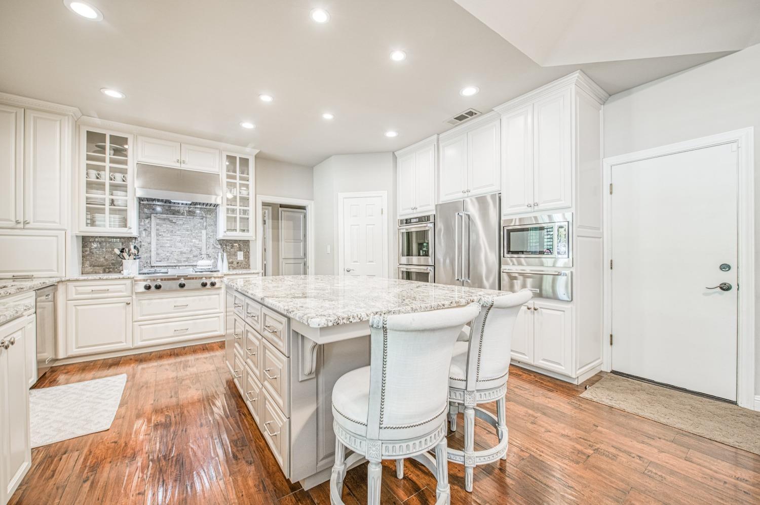 692 East Blue Ridge Road Fresno, CA 93725 - Photo 20 of 68 a kitchen with stainless steel appliances kitchen island granite countertop a stove a sink a refrigerator and white cabinets with wooden floor
