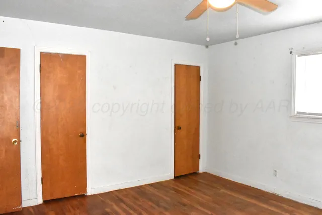 a view of an empty room with wooden floor and a ceiling fan
