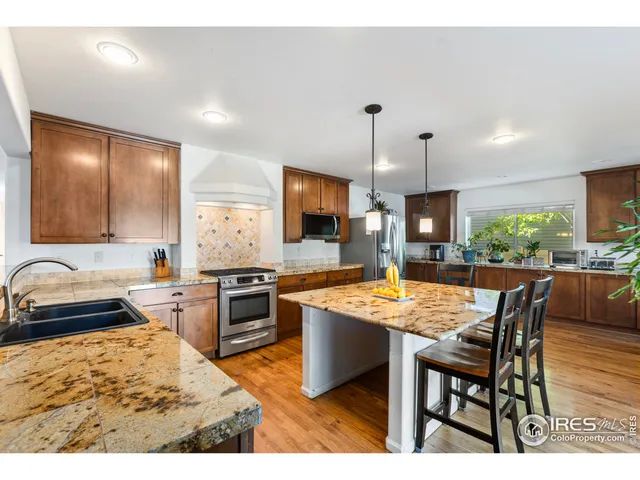 a kitchen with stainless steel appliances granite countertop a stove top oven a sink a dining table and chairs with wooden floor