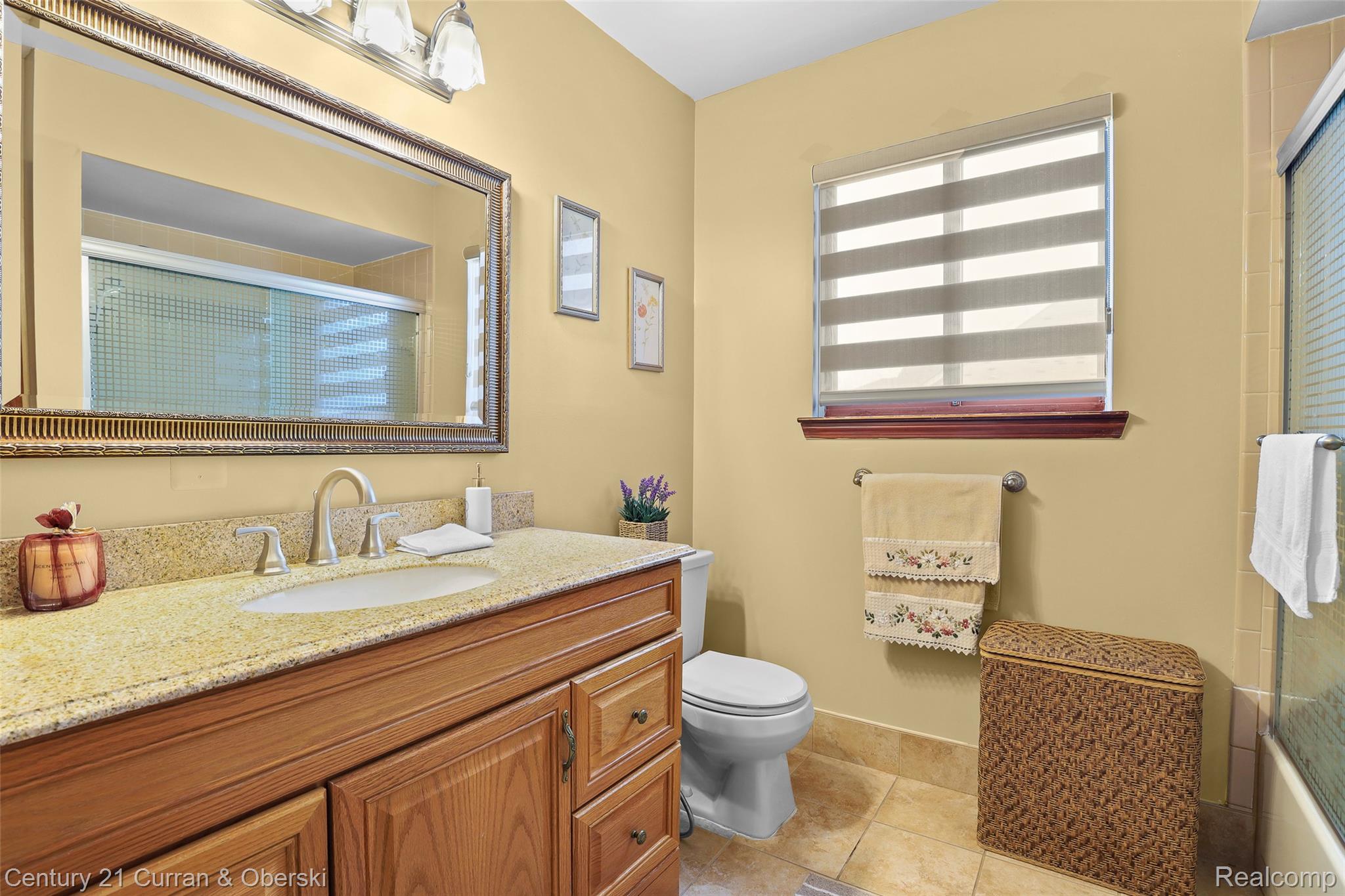 5296 Chase Road Dearborn, MI 48126 - Photo 14 of 36 Bathroom featuring a wood-finish vanity with a built-in sink and stone countertop, a decorative framed mirror, and a window with horizontal blinds