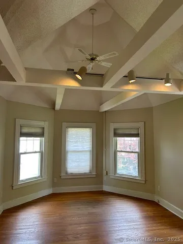 an empty room with wooden floor chandelier fan and windows