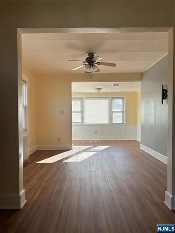 an empty room with wooden floor chandelier fan and windows