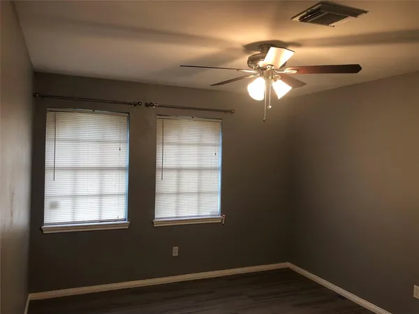 an empty room with wooden floor fan and windows