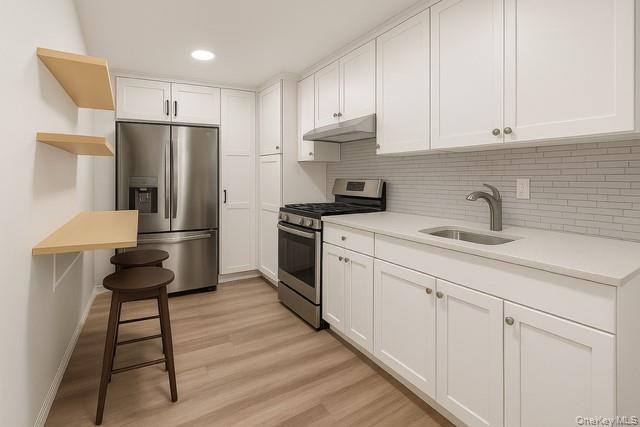 609 Palmer Road, Unit 3M Yonkers, NY 10701 - Photo 15 of 18 Virtually Staged kitchen featuring stainless steel appliances, white cabinetry, light wood-style flooring, under cabinet range hood, and backsplash