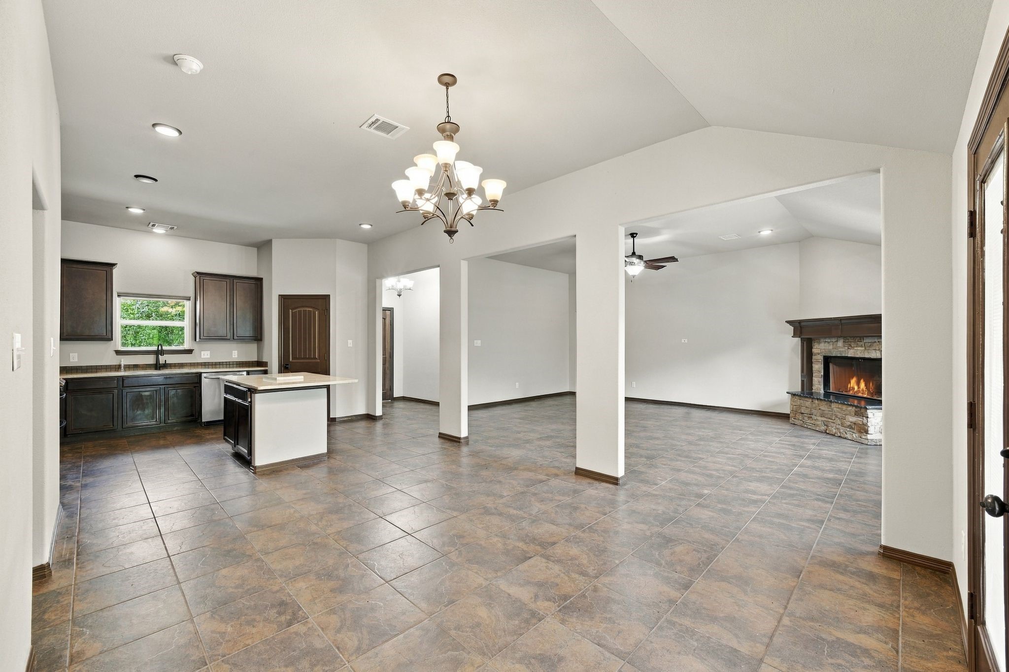 7049 Pine Shadows Road Cleveland, TX 77328 - Photo 10 of 49 Spacious open-concept living area with elegant tile flooring, featuring a cozy stone fireplace, modern kitchen with dark cabinetry, and a stylish chandelier for a warm, inviting atmosphere.