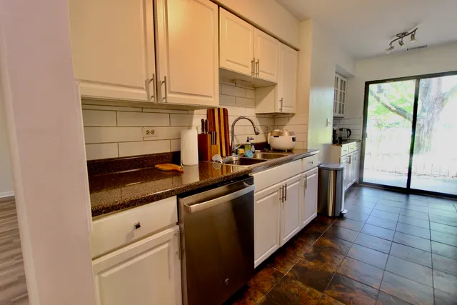 a kitchen with a sink dishwasher and white cabinets with wooden floor