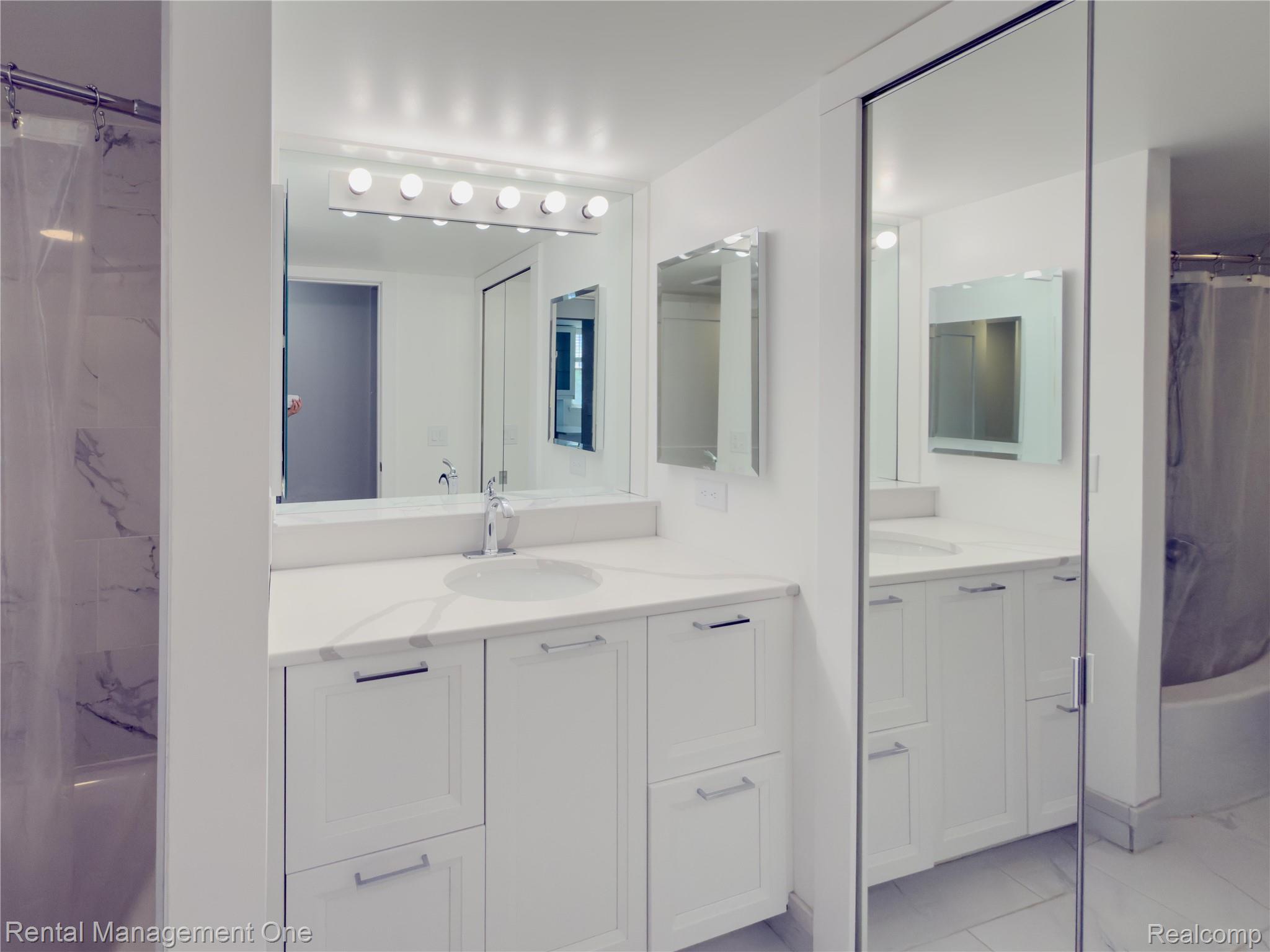 1603 Cass Lake Road, Unit D Keego Harbor, MI 48320 - Photo 10 of 20 Bright bathroom featuring a dual vanity with white cabinetry and integrated sinks, complemented by a large mirror and overhead vanity lighting