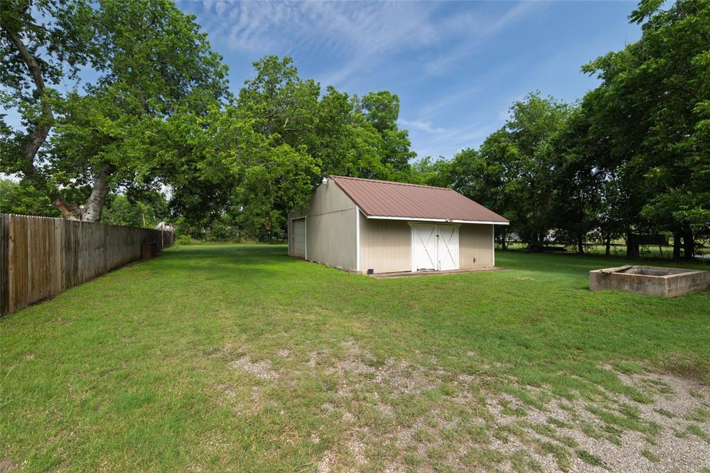 313 North Roe Street White Settlement, TX 76108 - Photo 29 of 33 Expansive yard featuring a detached storage building with a metal roof and double barn doors, a wooden privacy fence, mature trees, and a concrete planter box