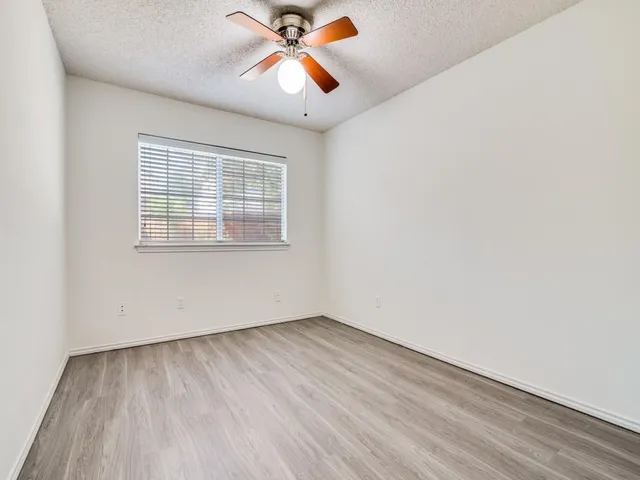 an empty room with wooden floor fan and windows