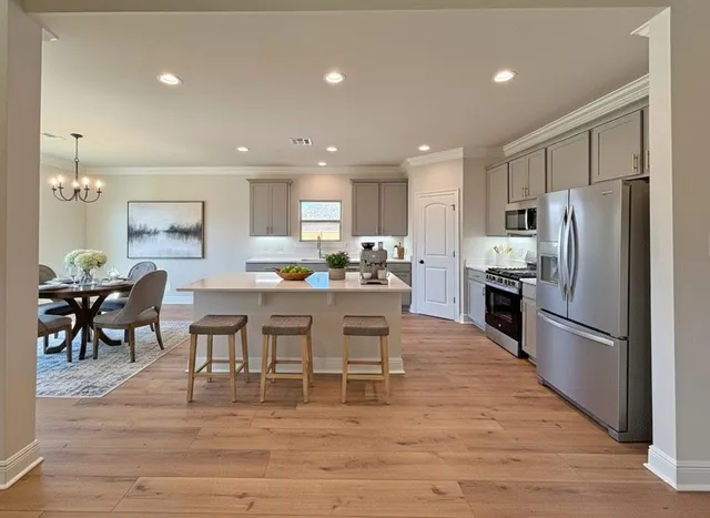 a kitchen with stainless steel appliances granite countertop a refrigerator a stove a sink a dining table and chairs with wooden floor