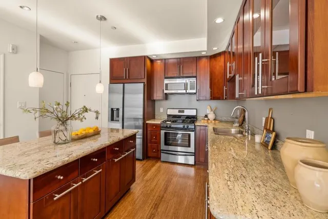 a kitchen with stainless steel appliances granite countertop a sink a stove and a wooden floors