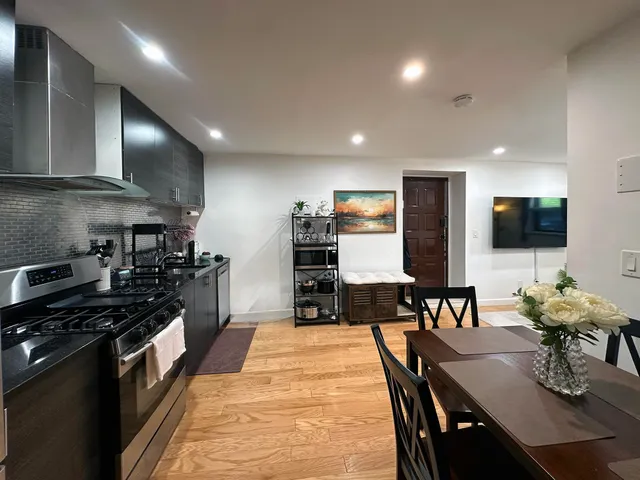 a kitchen with stainless steel appliances kitchen island granite countertop a stove a refrigerator a kitchen island a dining table and chairs with wooden floor