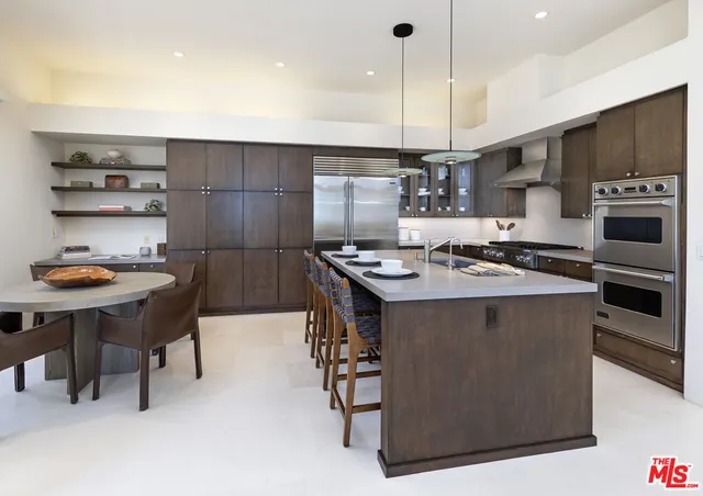 a kitchen with stainless steel appliances granite countertop a stove a refrigerator a sink a dining table and chairs with wooden floor