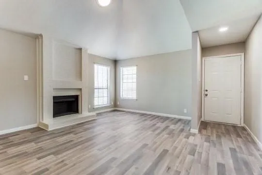 an empty room with wooden floor fireplace and windows