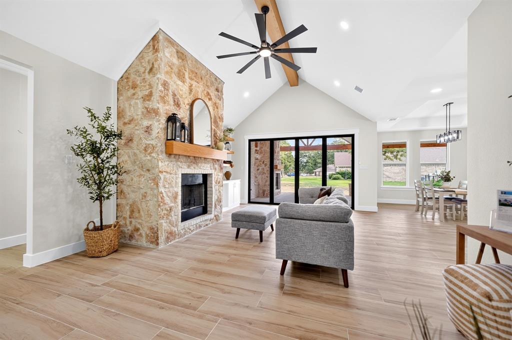 120 Springwood Road Enchanted Oaks, TX 75156 - Photo 9 of 37 Stone-clad fireplace with wood mantel, vaulted ceiling with exposed beam, wood-finish flooring, recessed lighting, and multi-panel sliding glass doors