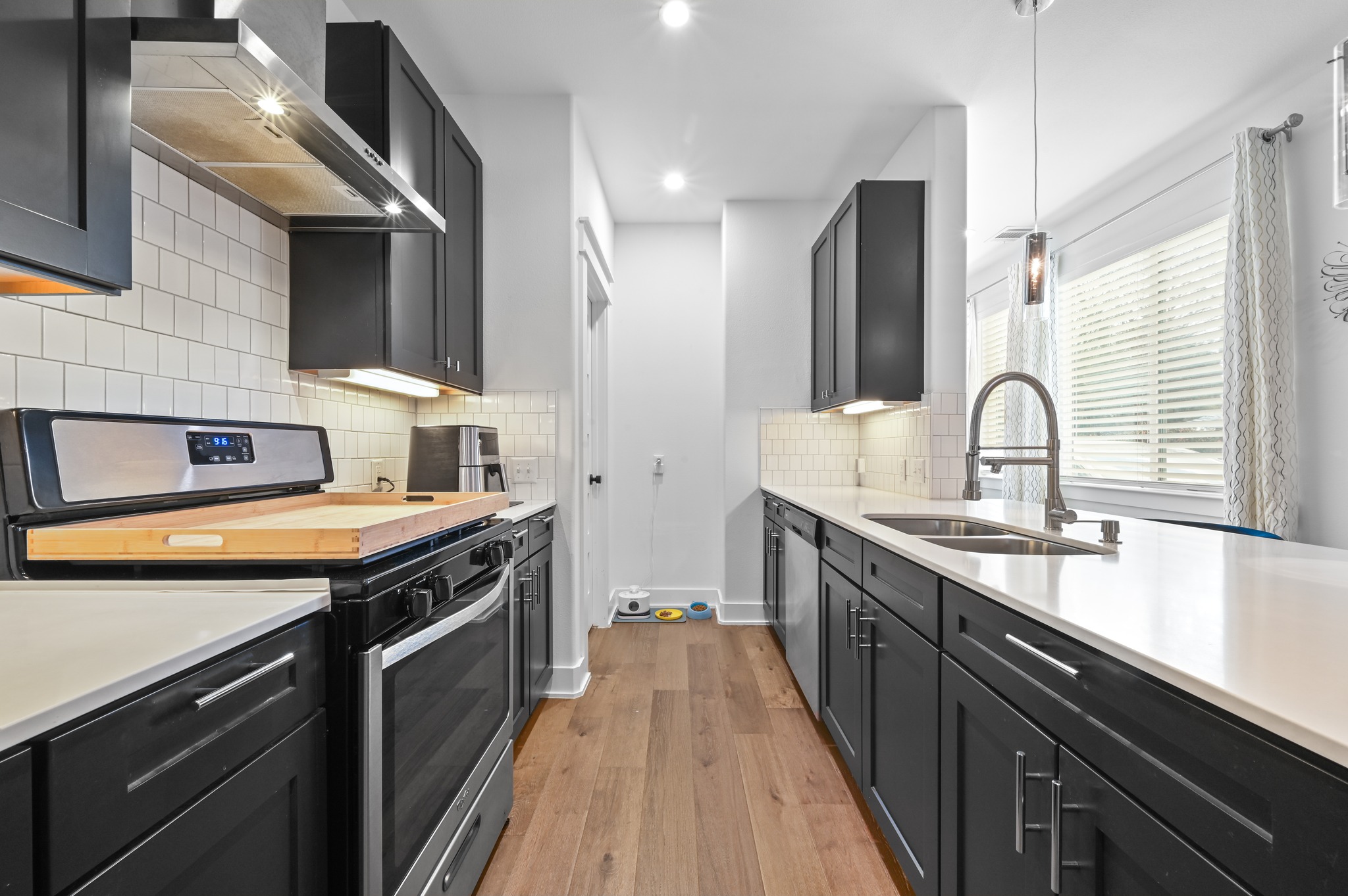 1405 Casey Street, Unit B Austin, TX 78704 - Photo 3 of 28 Kitchen with dark cabinetry, stainless steel appliances, light wood-style flooring, decorative backsplash, and light stone countertops