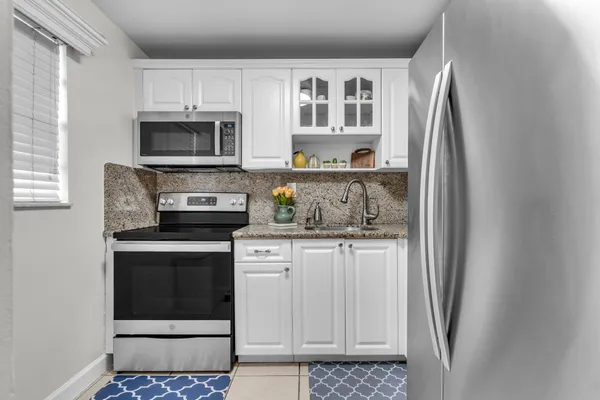 a kitchen with stainless steel appliances granite countertop a refrigerator a stove a sink and white cabinets with wooden floor