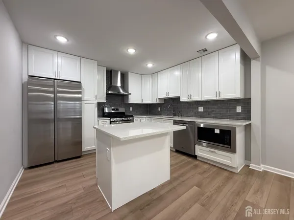 a kitchen with kitchen island granite countertop a refrigerator stove top oven and cabinets with wooden floor