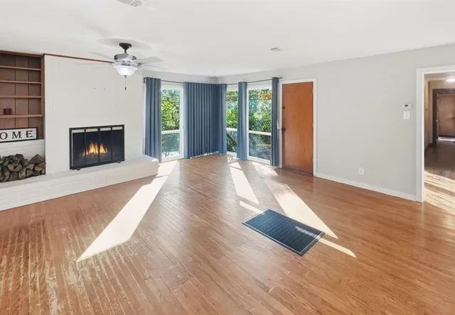 a view of an empty room with wooden floor fireplace and a window
