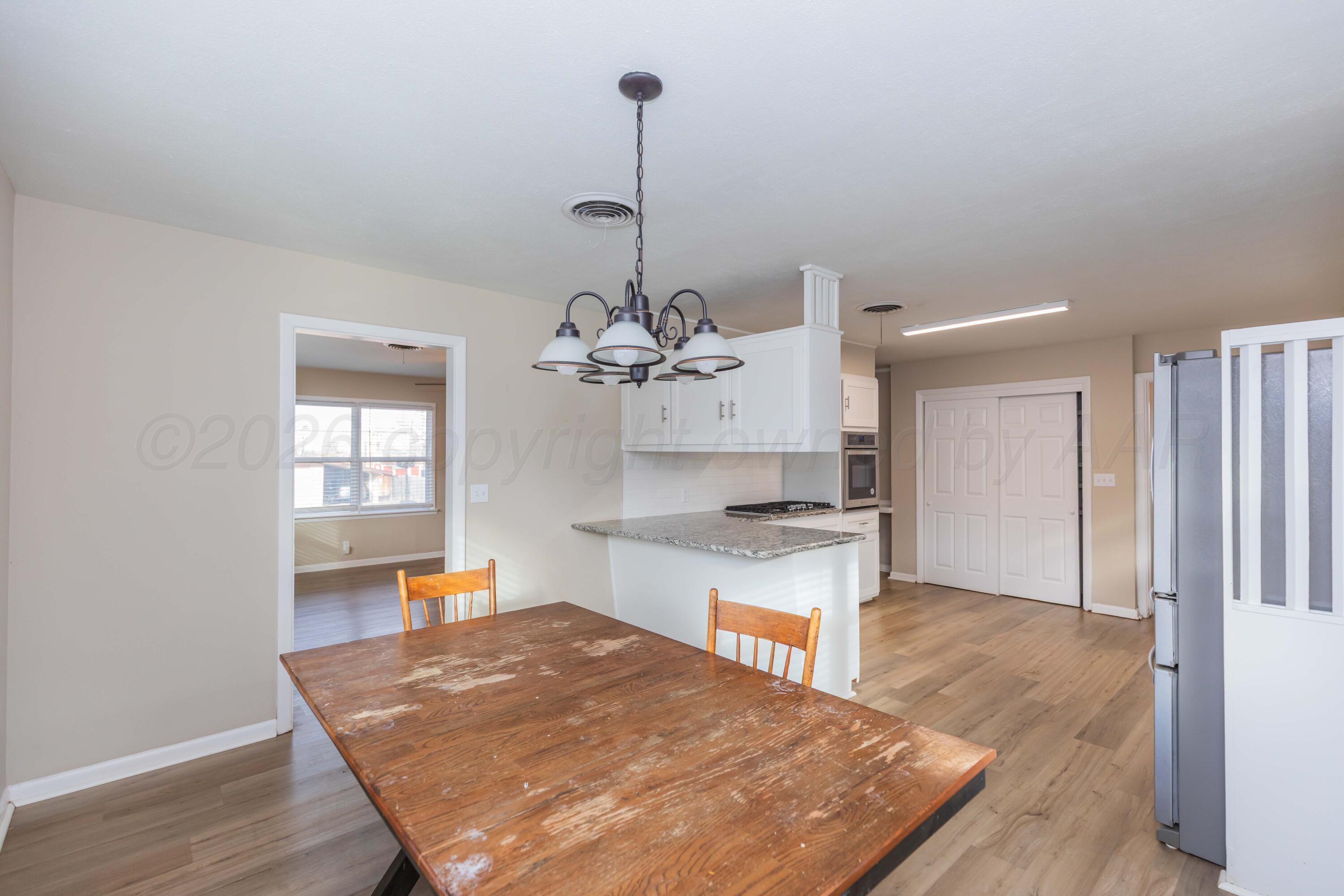 105 Smith Street Borger, TX 79007 - Photo 7 of 26 a large kitchen with kitchen island a stove a sink dishwasher a refrigerator and white cabinets with wooden floor