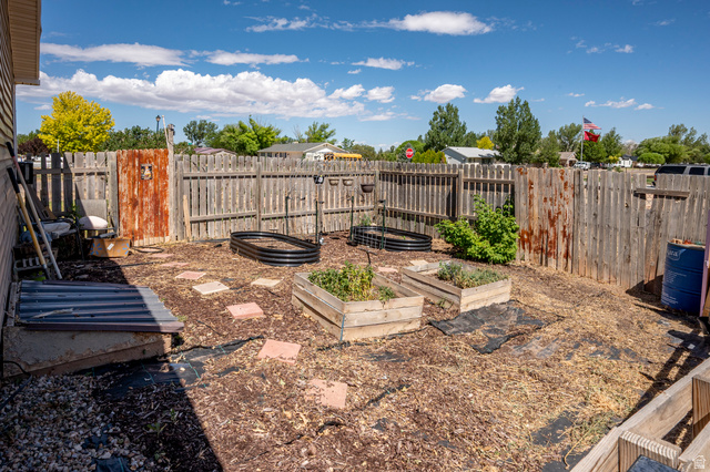 4296 Maple Lane Cedar City, UT 84721 - Photo 35 of 44 Fenced backyard featuring multiple raised garden beds, wood chip ground cover, and a combination wood and corrugated metal privacy fence
