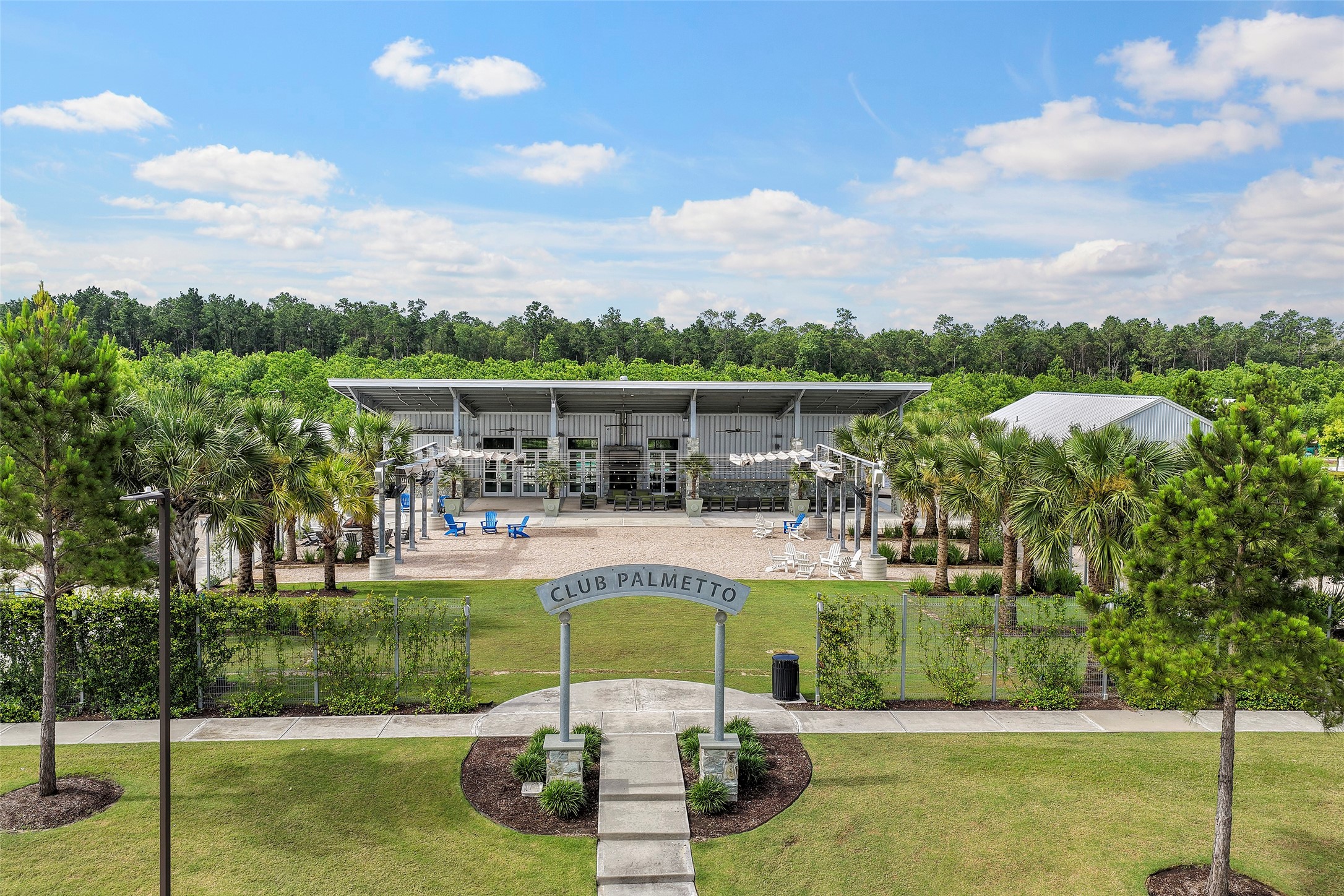 10603 Whitejacket Conroe, TX 77385 - Photo 33 of 42 This photo showcases a modern clubhouse, "Club Palmetto," surrounded by lush greenery and palm trees. The facility features outdoor seating and a spacious, inviting ambiance, perfect for community gatherings.