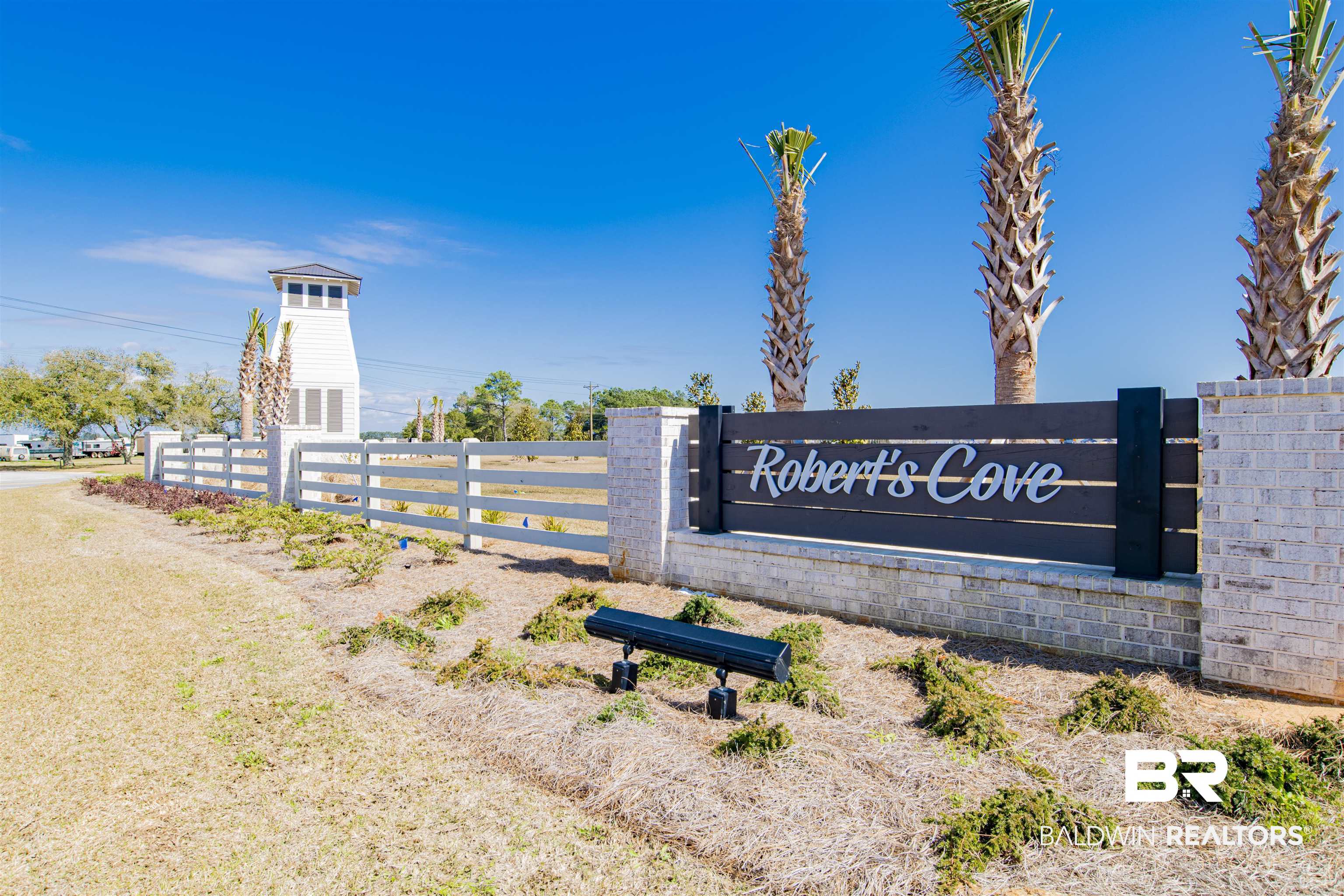 22301 Early Dawn Circle Foley, AL 36535 - Photo 44 of 45 Entryway signage for "Robert's Cove" featuring a white painted fence, brick columns, and a coordinating dark wood-finish sign