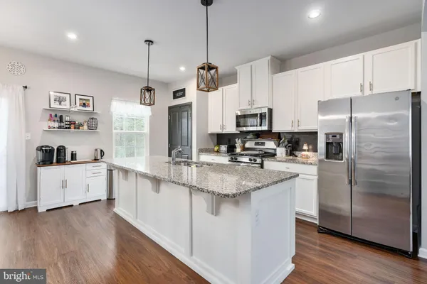 a kitchen with stainless steel appliances kitchen island granite countertop a refrigerator a sink dishwasher a stove and white cabinets with wooden floor