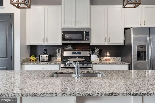 a view of kitchen with stainless steel appliances granite countertop a stove a refrigerator a sink and white cabinets