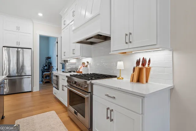 a kitchen with stainless steel appliances granite countertop a refrigerator a stove a sink and white cabinets