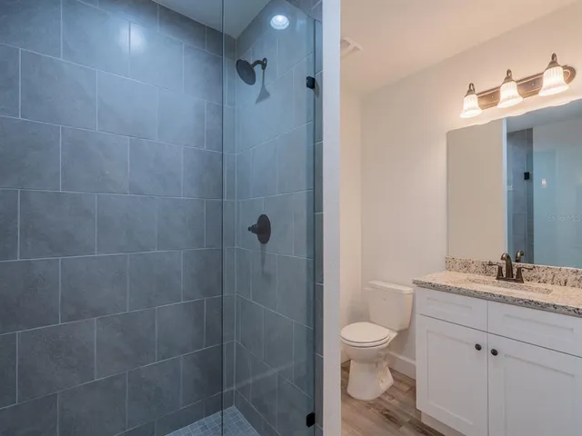 a bathroom with a granite countertop toilet a sink a mirror and shower