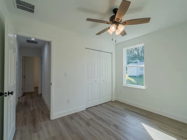 an empty room with wooden floor fan and windows