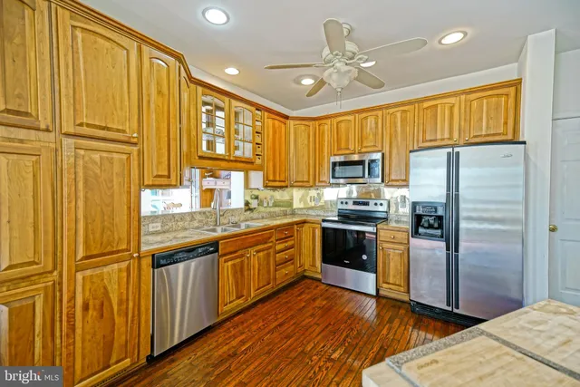 a kitchen with stainless steel appliances granite countertop a refrigerator a sink dishwasher a stove and a dining table with wooden floor