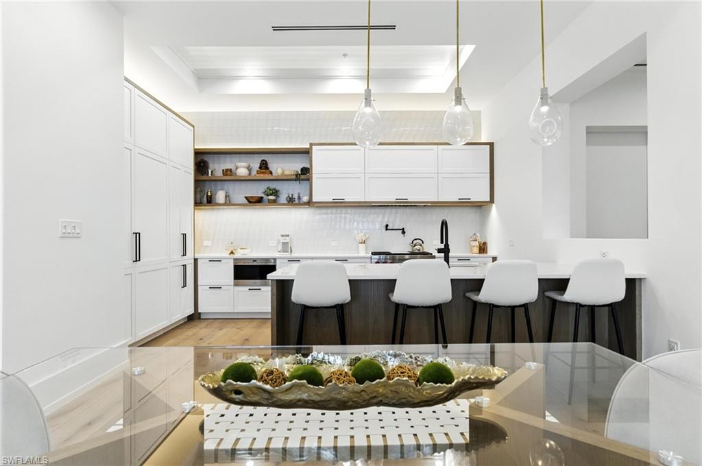 201 8th Street South, Unit 208 Naples, FL 34102 - Photo 12 of 39 Kitchen with tasteful backsplash, a breakfast bar, light countertops, white cabinetry, and light wood finished floors