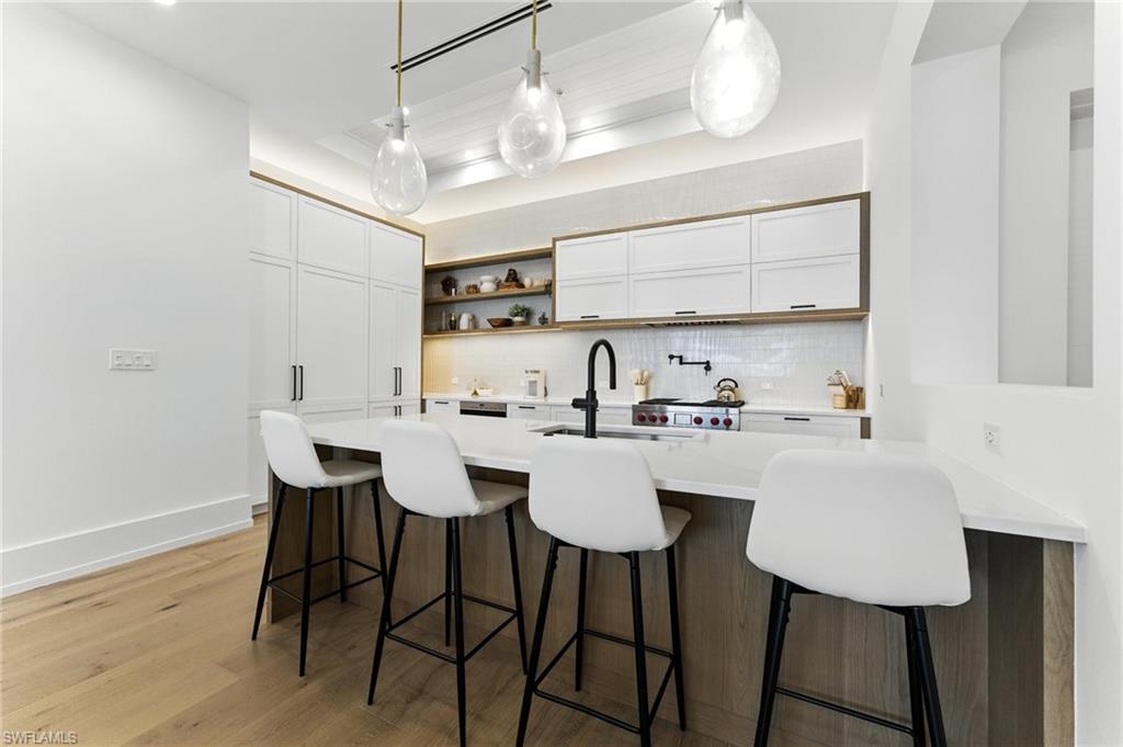201 8th Street South, Unit 208 Naples, FL 34102 - Photo 13 of 39 Kitchen featuring decorative backsplash, light countertops, open shelves, a breakfast bar, and white cabinetry
