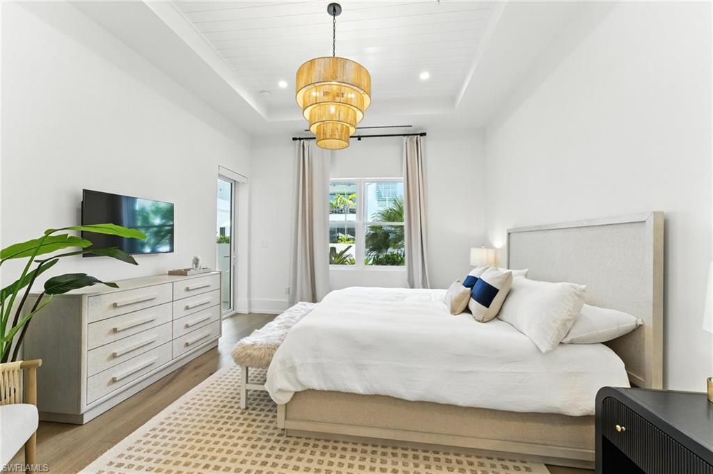 201 8th Street South, Unit 208 Naples, FL 34102 - Photo 14 of 39 Bedroom featuring a tray ceiling, light wood finished floors, a chandelier, recessed lighting, and access to exterior, IMPACT WINDOWS AND DOORS, 2 walk-in closets in hallway