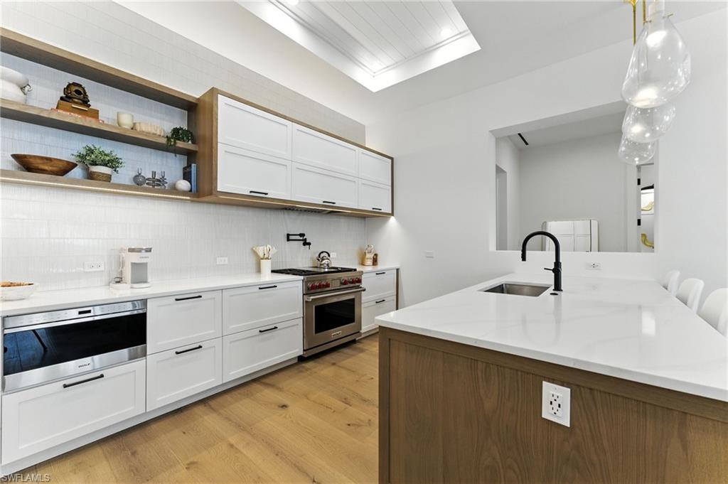 201 8th Street South, Unit 208 Naples, FL 34102 - Photo 9 of 39 Kitchen featuring designer range, light wood-style floors, tasteful backsplash, white cabinets, and light stone counters