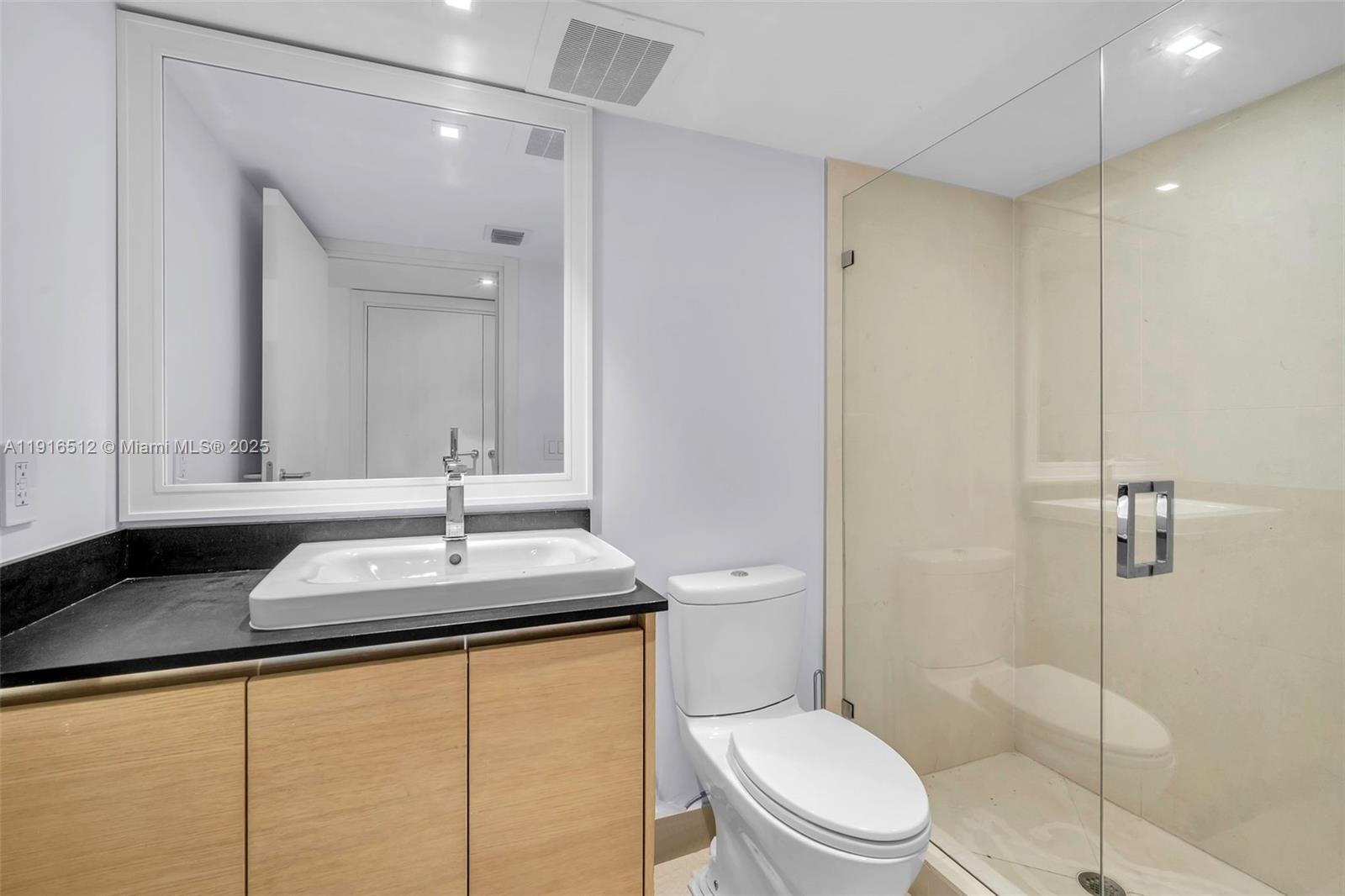 9501 Collins Avenue, Unit 1 Surfside, FL 33154 - Photo 52 of 53 a bathroom with a granite countertop sink toilet mirror and a shower