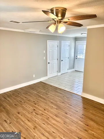 a view of an empty room with wooden floor and a ceiling fan