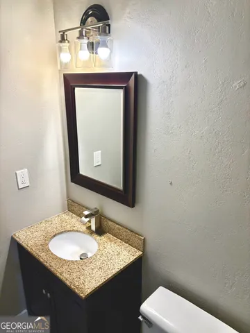 a bathroom with a granite countertop toilet a sink and a mirror