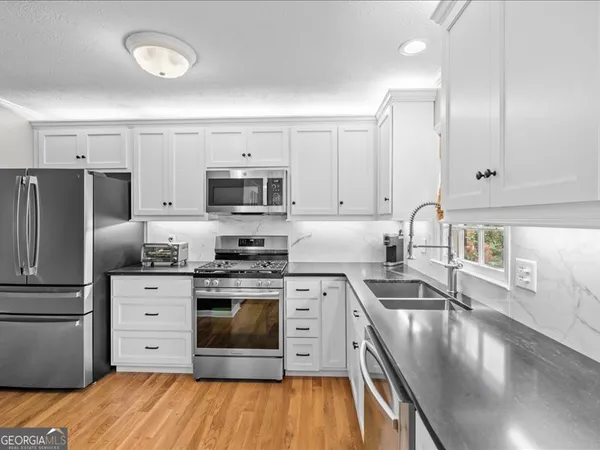 a kitchen with stainless steel appliances granite countertop a stove top oven a sink dishwasher and a refrigerator with wooden floor