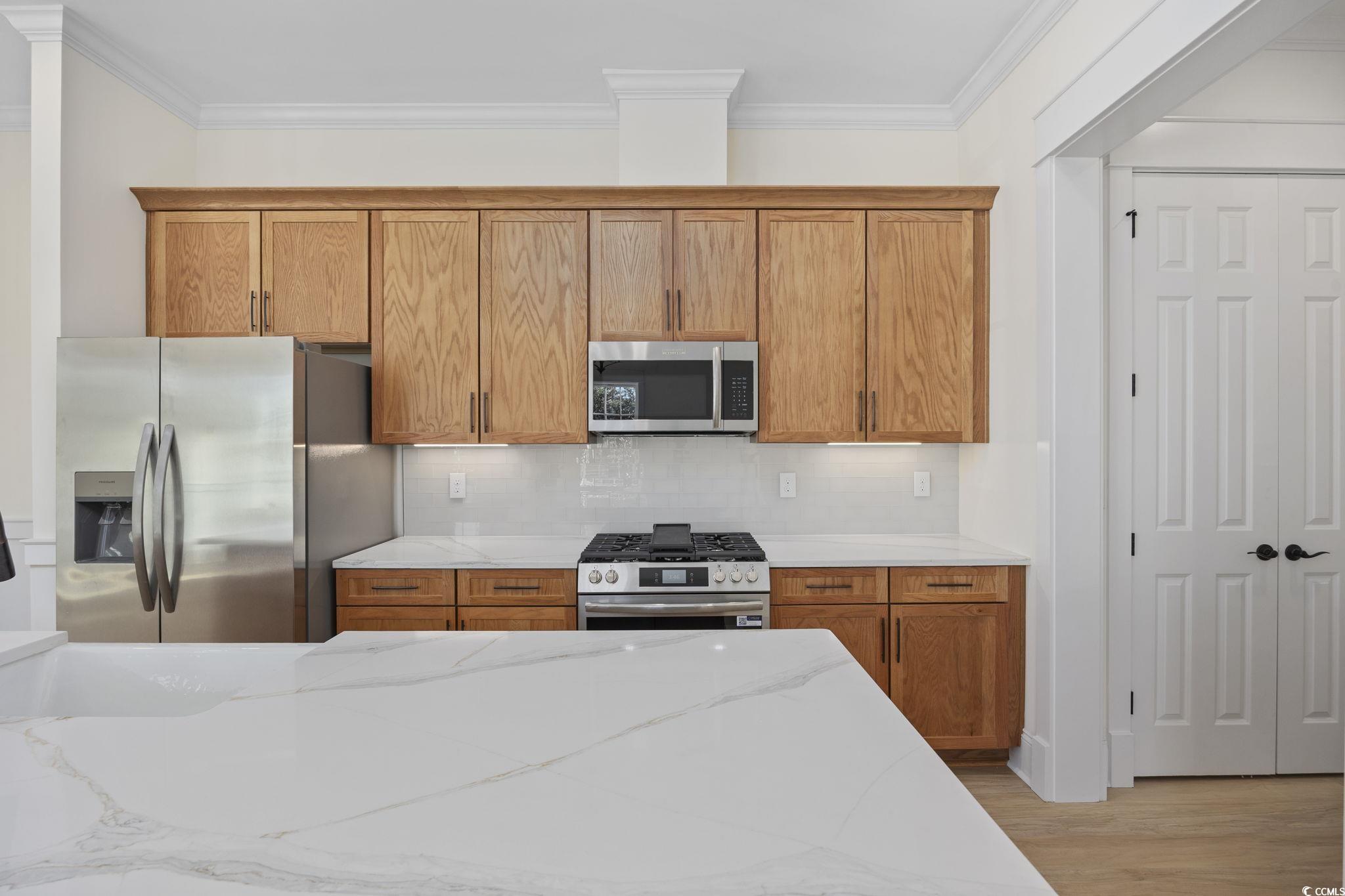 965 Hackler Street, Unit E Myrtle Beach, SC 29577 - Photo 7 of 36 Kitchen featuring stainless steel appliances, brown cabinets, light stone countertops, backsplash, and light wood-style floors