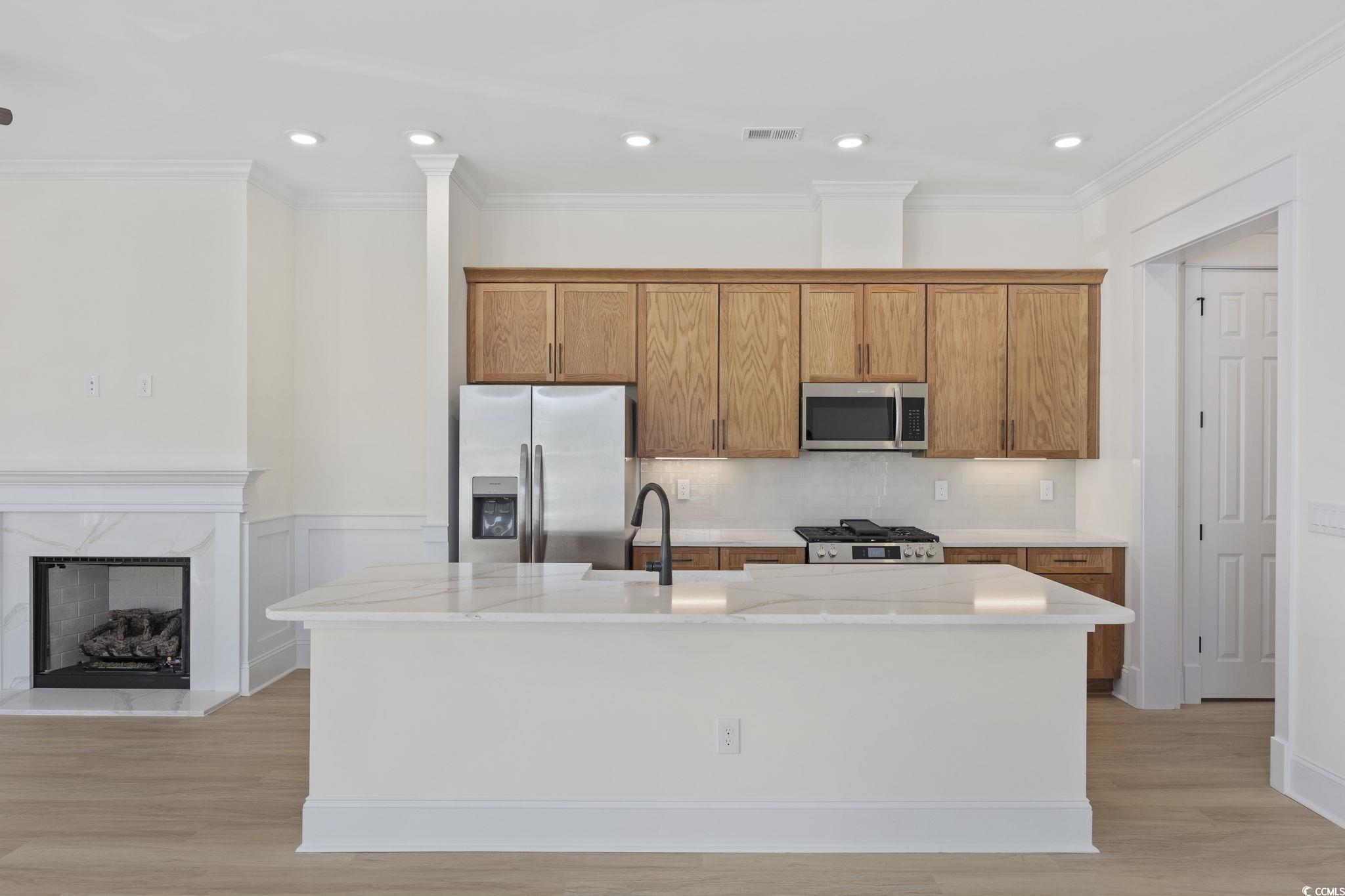 965 Hackler Street, Unit E Myrtle Beach, SC 29577 - Photo 9 of 36 Kitchen with appliances with stainless steel finishes, brown cabinetry, an island with sink, backsplash, and light stone counters