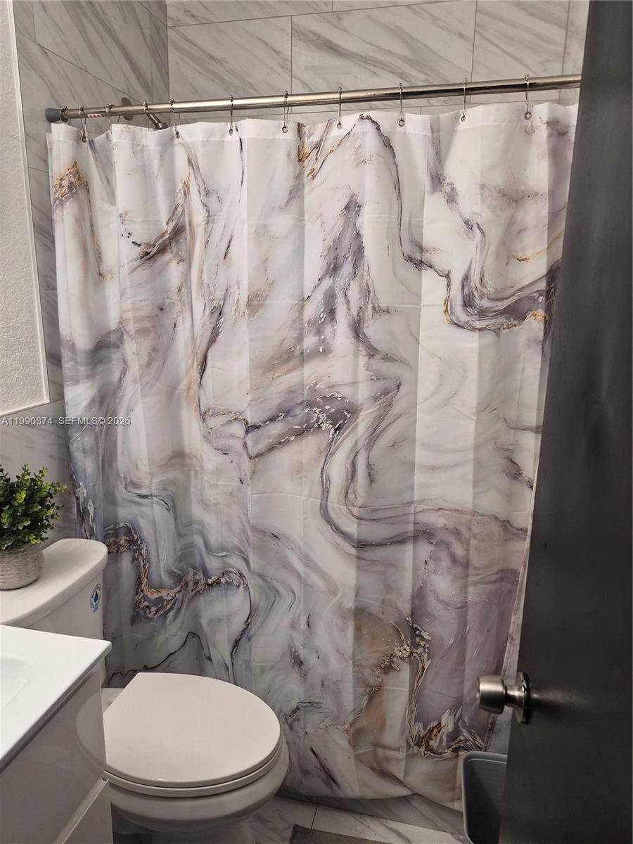 6117 Southwest 31st Street, Unit B Miramar, FL 33023 - Photo 7 of 8 a white toilet sitting next to a shower curtain