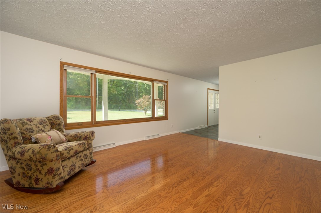 Living area with wood finished floors, a textured ceiling, and baseboard heating
