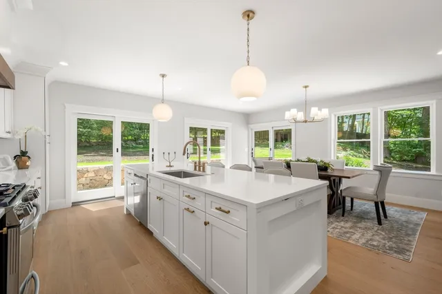 a kitchen with stainless steel appliances kitchen island granite countertop a stove a sink a refrigerator and white cabinets with wooden floor