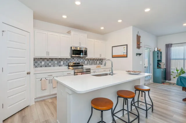 a kitchen with a sink a stove a refrigerator and white cabinets with wooden floor