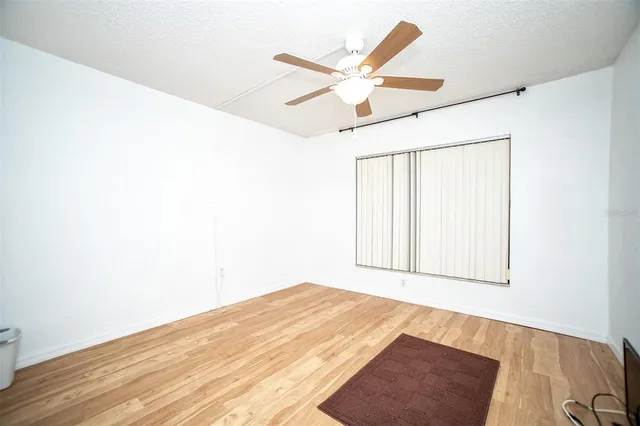 an empty room with wooden floor fan and windows